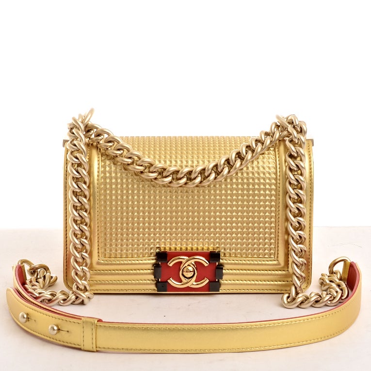 Chanel gold embossed lambskin leather Cube Boy flap bag with matte goldtone hardware, front flap with red and black enamel CC push lock closure and matte goldtone chain link and gold/red leather padded shoulder strap. Interior is lined in navy