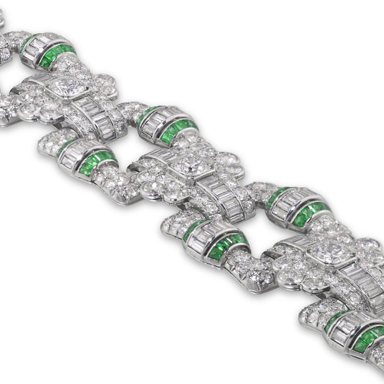 An important French Art Deco emerald and diamond open panel bracelet, the bracelet comprised of six square open panels of a geometric design, with fancy lozenge-shaped links, set throughout with brilliant- and baguette-cut diamonds, estimated to