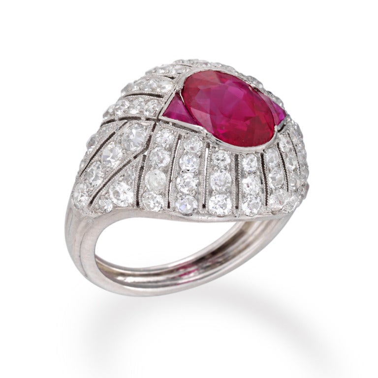A French Art Deco ruby and diamond ring, the central oval faceted ruby weighing 3.88 carats, accompanied by report stating its origin to be from Mogok, Burma, set between two triangular-shaped straight-side faceted rubies weighing a further total of