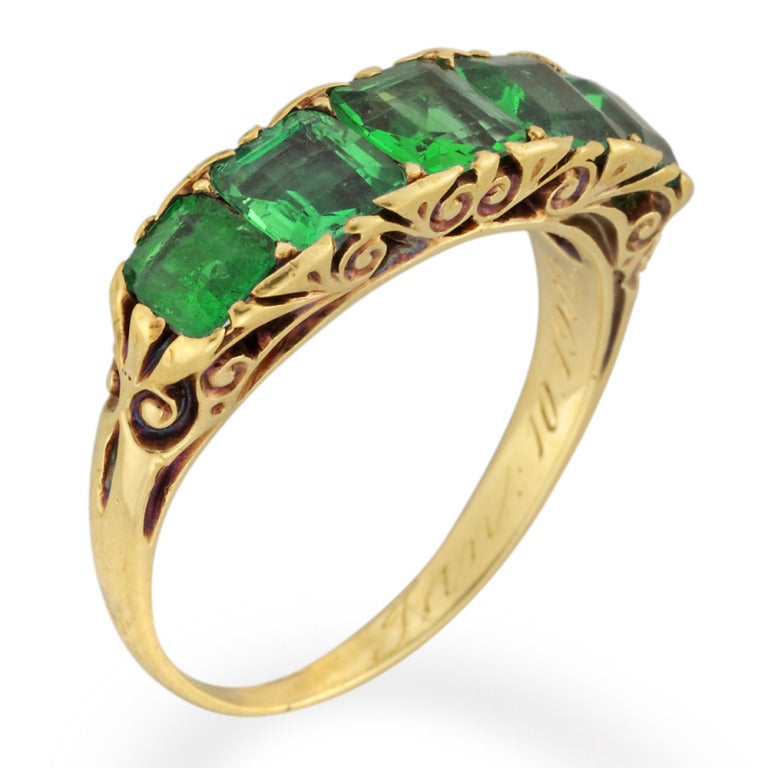 A Victorian five stone emerald carved half hoop ring, the ring set with five square emerald-cut emeralds, estimated to weigh a total of 1.7 carats, all claw-set to an ornate scroll carved yellow gold gallery and shoulders, all to a tapered D-section