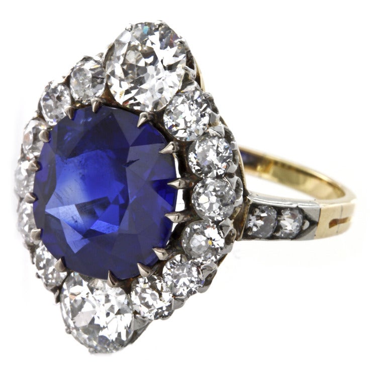 A turn-of-the-century Burmese sapphire and diamond cluster ring, the central round-shaped faceted sapphire weighing 4.84 carats, accompanied by GAGTL certificate stating to be of Burmese origin with no indication of heating, to a graduated cluster