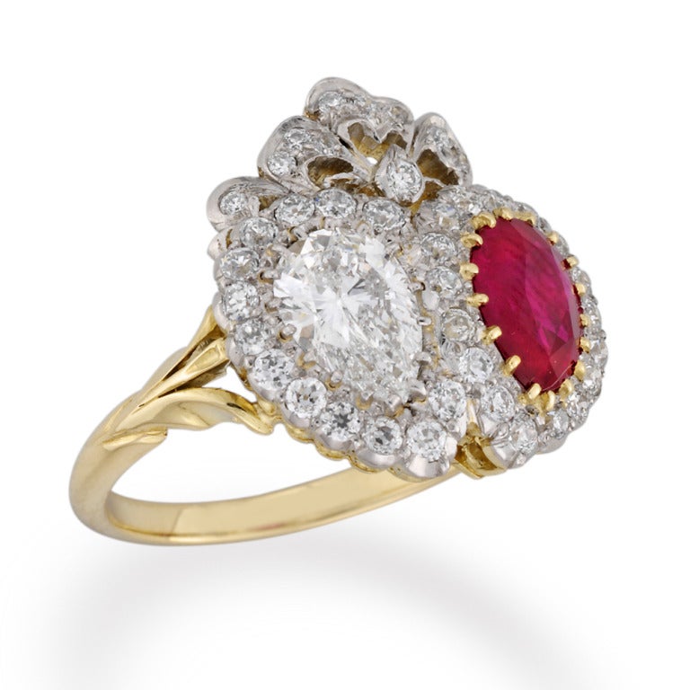 A diamond and ruby ring, the ring in the form of a double heart, set with a pear-shaped diamond and a faceted ruby of similar shape, estimated to weigh 0.84 carats and 1.28 carats, to the centre of a diamond cluster surround and ribbon bow surmount,