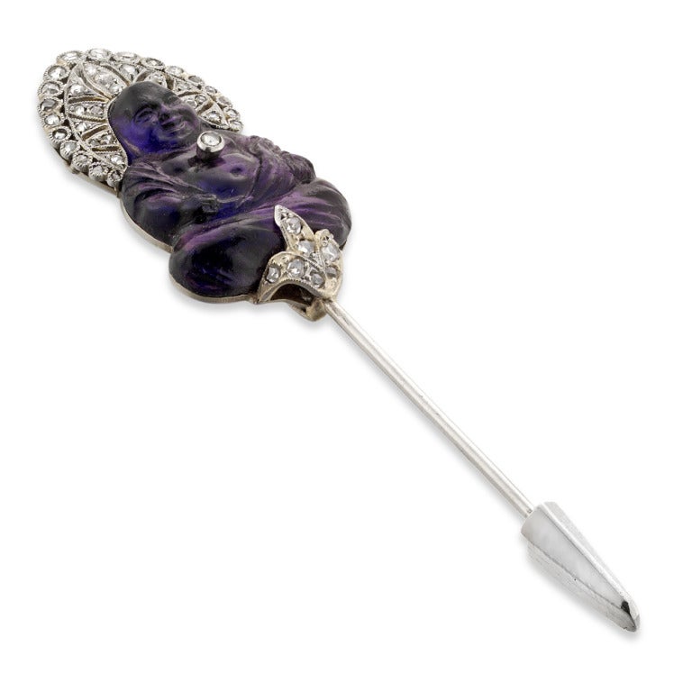 A LaCloche Art Deco amethyst buddha pin, the pin comprising a carved amethyst buddha, embellished with rose-cut diamond-set halo, centre and fleur-de-lis base, all set to a platinum mount and pin, signed LaCloche Freres, gross weight 6.6 grams,