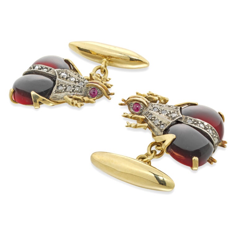 A pair of garnet and diamond beetle cufflinks, each beetle set with two cabochon-cut segments and rose-cut diamonds to the body, with yellow gold head and legs and ruby cabochon eyes, to a chain link connection and baton fastening.