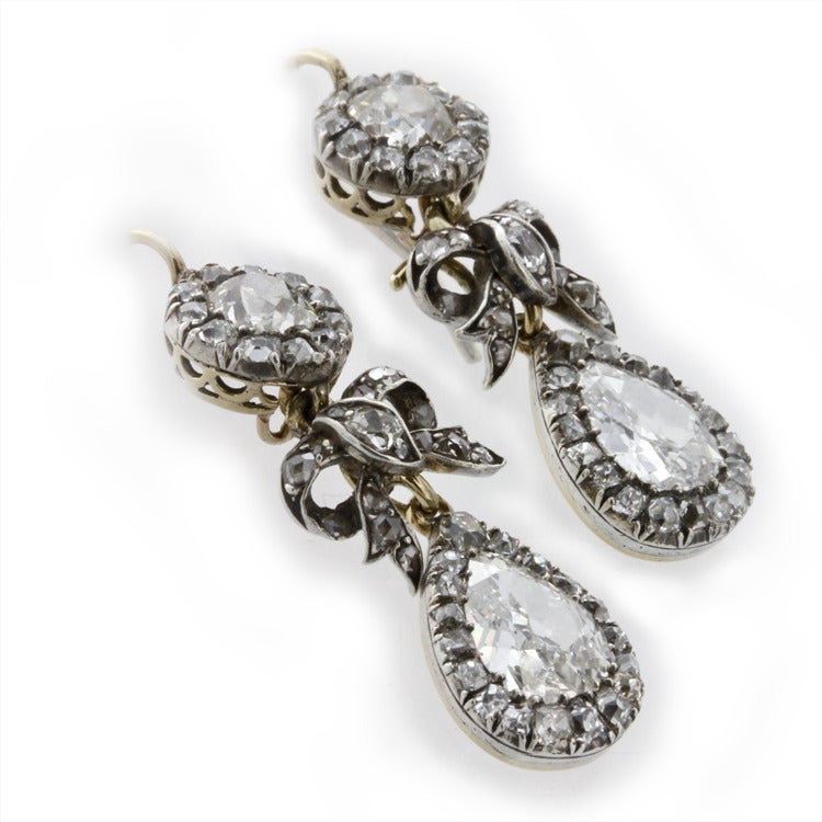 A pair of Early Victorian diamond drop earrings, each earring comprising a circular diamond cluster surmount, and pear-shaped diamond cluster drop, linked by a diamond-encrusted ribbon bow, diamonds estimated to weigh a total of 3.60 carats for both