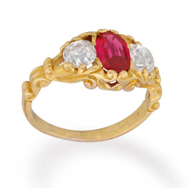 A Victorian three stone ruby and diamond ring, the oval faceted ruby weighing an estimated 0.70 carats set between two old brilliant-cut diamonds weighing approximately 1 carat in total all to a scrolled pierced yellow gold mount, circa 1870.