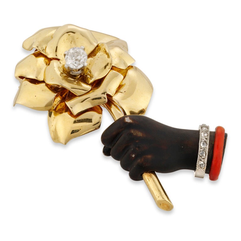 Flower and hand motif brooch by Cartier, comprising a black enamelled hand and wrist with one bangle set with seven rose diamonds in platinum millegrain settings and a second red enamel bangle, the hand clasping a polished gold flower with ten