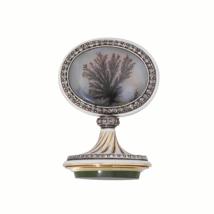 A Faberge' jewelled and enamelled gold and hardstone seal, the flat oval handle inset at both sides with a moss agate panel over sunburst engine-turning within a rose-cut diamond-set border, the mount enamelled in opaque white, the collar with