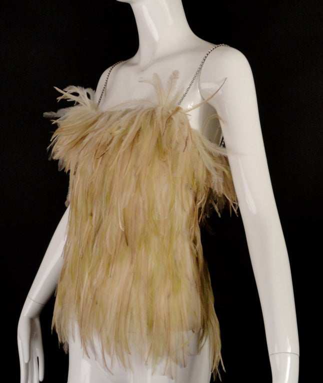 Early 1990s top in ivory silk organza with snap closures down the side. The top is covered in ivory/ecru feathers that spray off the top but lie flat down the body. Spaghetti straps in single strands of sparkling rhinestones.