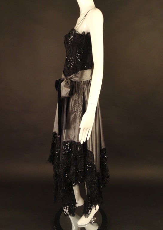 Stunning 1970s evening gown in a pewter silk taffeta and black lace. The gown has a dart fitted bodice in black silk and covered in a black spider web lace that is then adorned in crystal organza ribbon work and black sequins. The skirt falls in