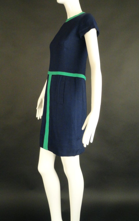 Late 1960s dress in navy linen and accented with green. The dress has a scoop neckline with darts falling from under the bust to the waistline. Short, set in sleeves end with a turned under finish. The slender skirt falls from the green appliqué