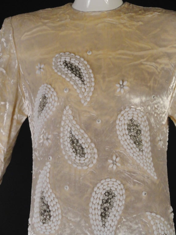 1980s Evening gown in a ivory pane velvet with golden undertones. Gorgeous paisley shaped beading in faceted white glass beads and filled with silver and clear crystals. The gown is also dotted with tiny flowers in white glass and crystal beads. 