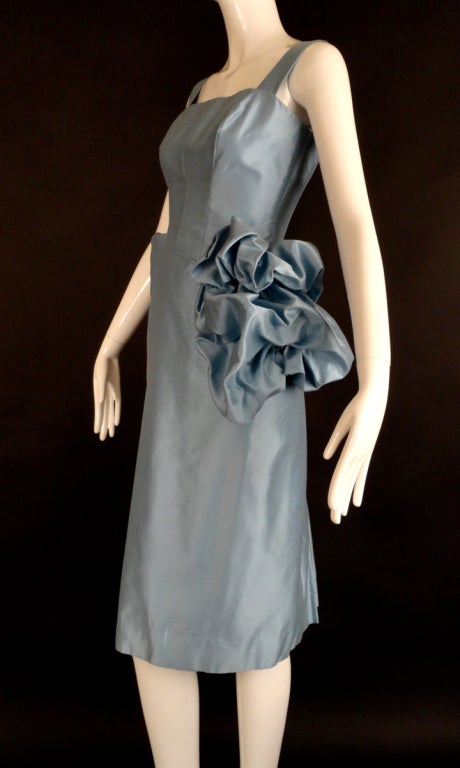 Fabulous 1950s wiggle dress in a powder blue, sharkskin alaskine. The dress is dart fitted through the bust to the diagonal waistline seam.  The skirt creates a draped, inset pocket on the right hip. Large gathered bubble flounce down the left hip.