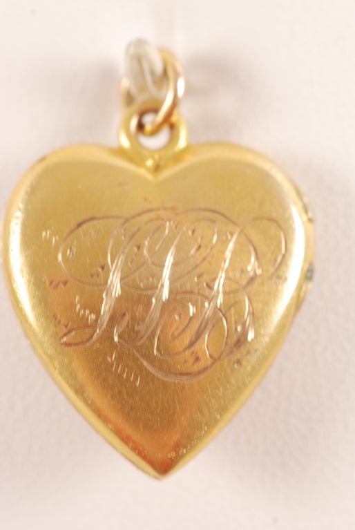 14k gold Victorian heart shaped locket with a diamond, sapphire and ruby set in a raised leaf. The front has exquisite, deep repoussse work. The rear has three initials done in exquisite hand engraving. Inside there is room for two photos or