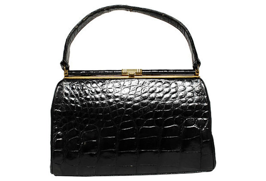 Black alligator handbag with goldtone clip clasp, feet and frame. Peach-colored leather lining with three pockets, one of them zippered. Loose mirror. Signed “Bellestone.” Handle 15”L.