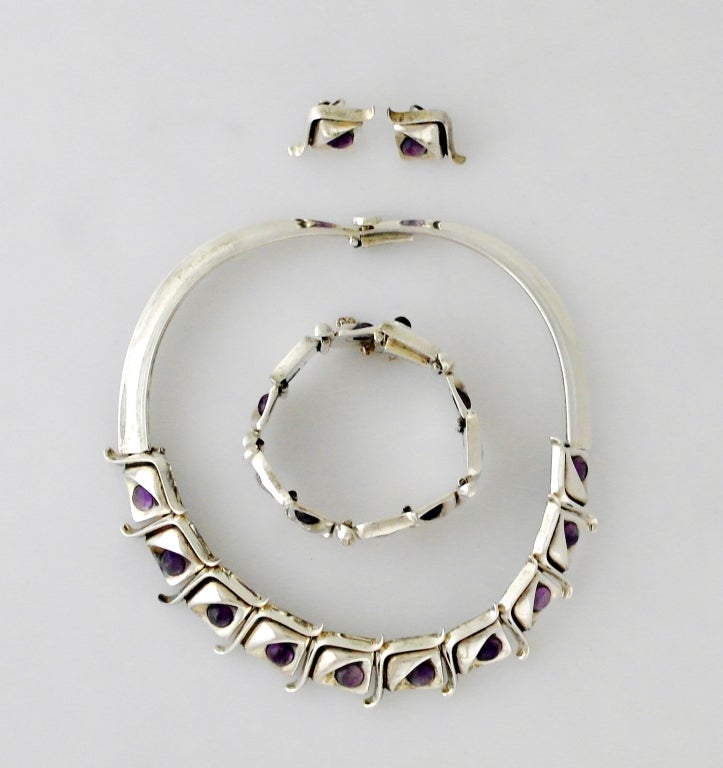 Being offered is a circa 1960s jewelry suite by one of Antonio Pineda's silversmiths of Taxco, Mexico, of .970 silver and cabachon amethysts.  Comprising a choker necklace, link bracelet and lever-back earrings, links adorned with the dimple wave