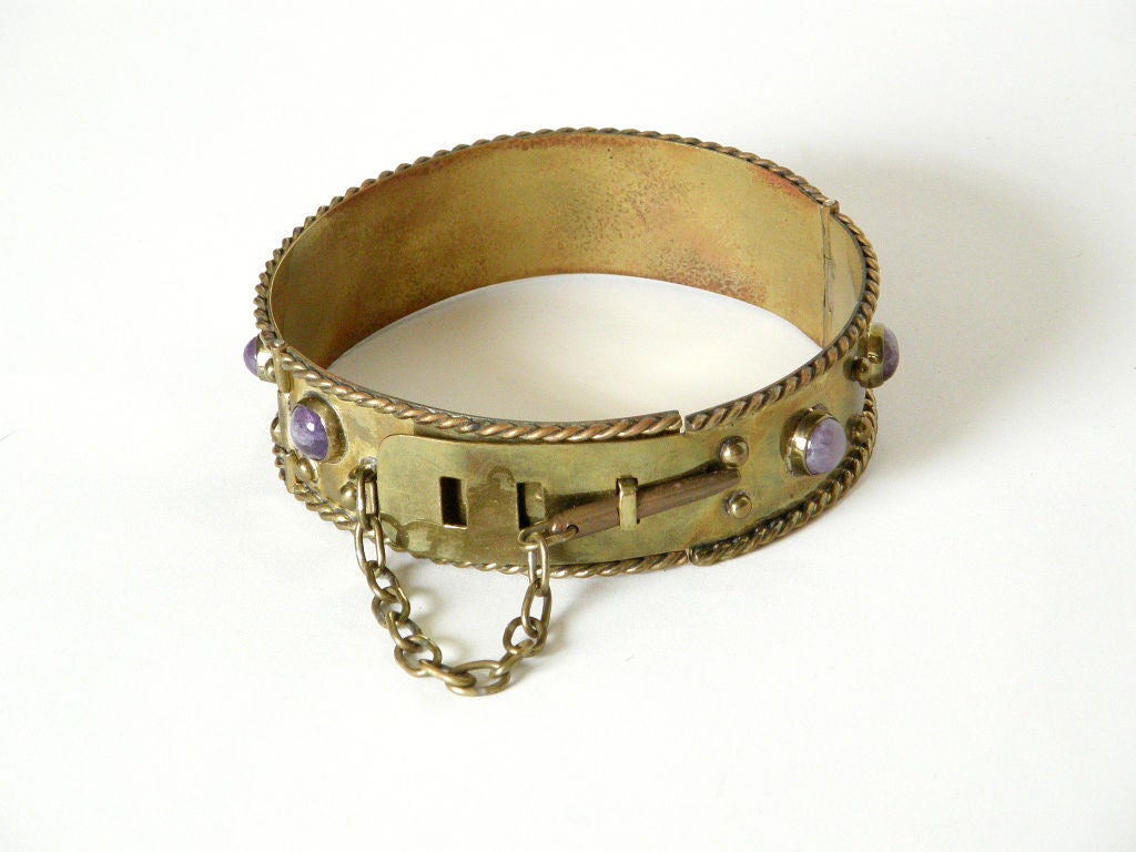 This dog collar style choker necklace is stylishly fierce. It's decorated with domed brass studs and large, cabochon amethysts, and it's trimmed with a twisted ropelike edge. The brass band is adjustable and is held in place with a pin on a