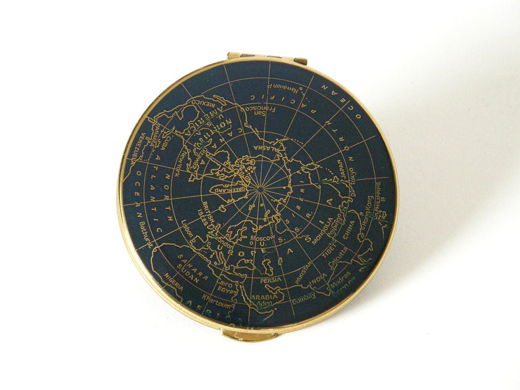 This unused compact is decorated like the globe with a map of the world embossed on it. Though it's flat, the decoration gives it the look of being spherical. The background is a midnight blue enamel, and it retains its protective cloth sleeve. It