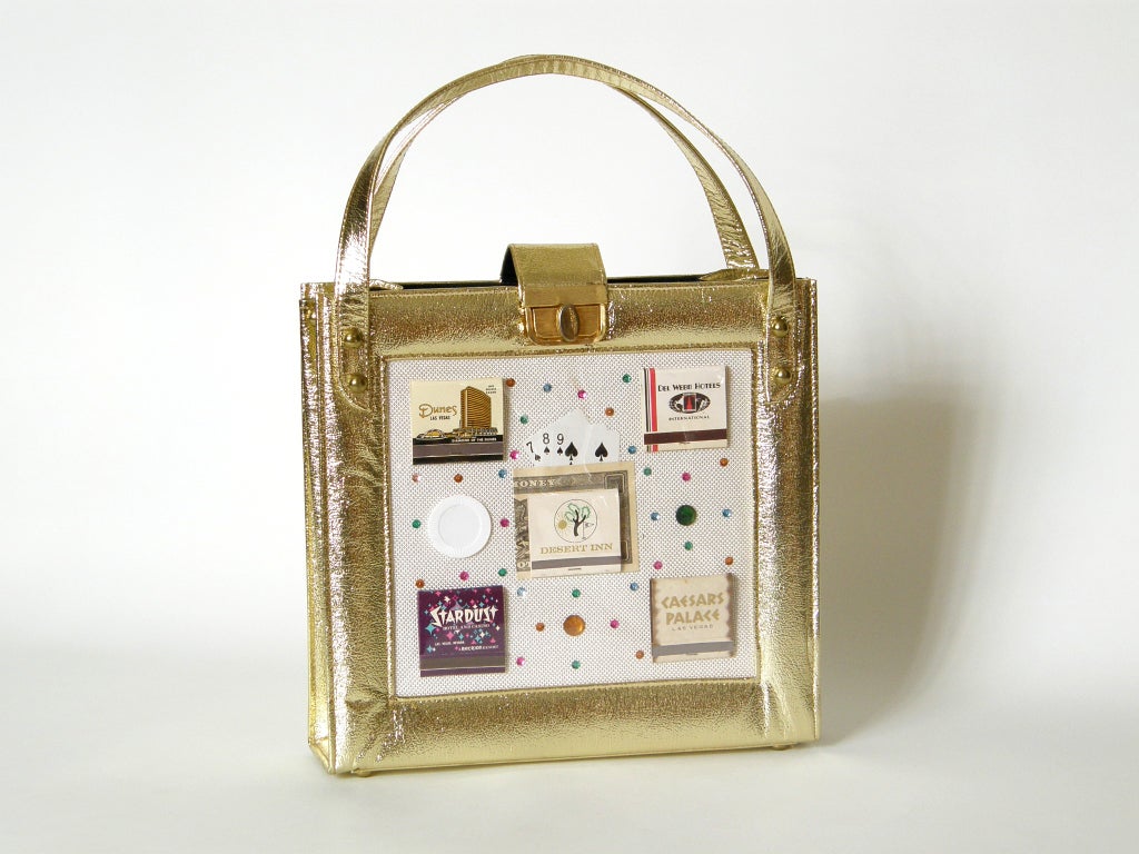 This whimsical, Las Vegas theme handbag has a textured gold vinyl body. On the front is a clear vinyl covered panel displaying casino matchbooks, cards, a poker chip and fake money with multicolored rhinestones scattered around them.

measures