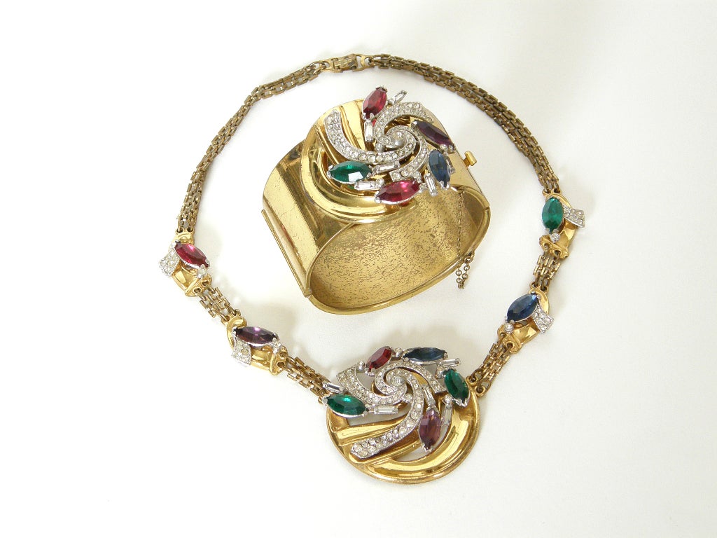 This lovely necklace and bracelet set was designed by McClelland Barclay. Both pieces feature a spiraling design of clear and colored rhinestones on a circular mount. The necklace has a square link chain separating the large pendant and the smaller