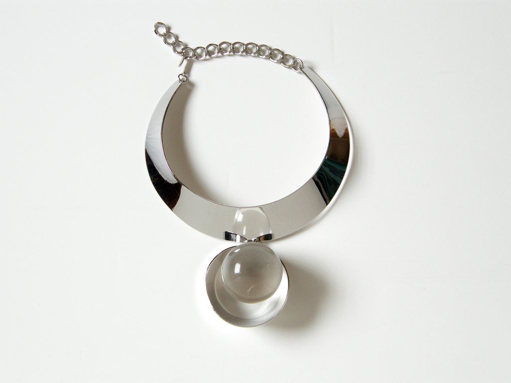 This Trifari collar and pendant has a bold 3-dimensionality and a futuristic style. The chrome neck ring bends one way, and the chrome ring around the lucite ball bends the other way. This play of convex and concave forms combine with the lucite