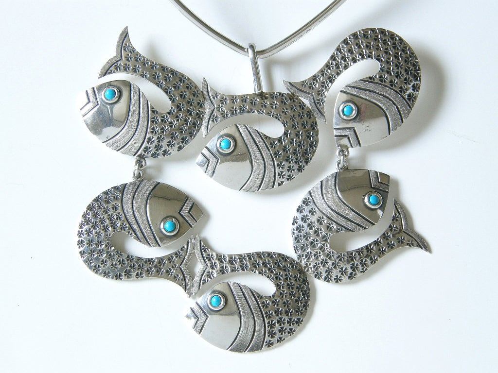 This Mexican sterling necklace has an oversized pendant made up of silver fish with turquoise eyes. The two rows of stylized fish are hinged together to add movement and to make this large scale necklace more comfortable to wear. The details of the