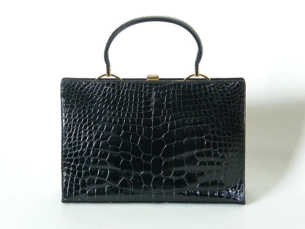 This classic black alligator handbag by Harry Rosenfeld has a lipstick red leather interior with one zippered pocket and two large and one small slip pockets. It measures 12.25