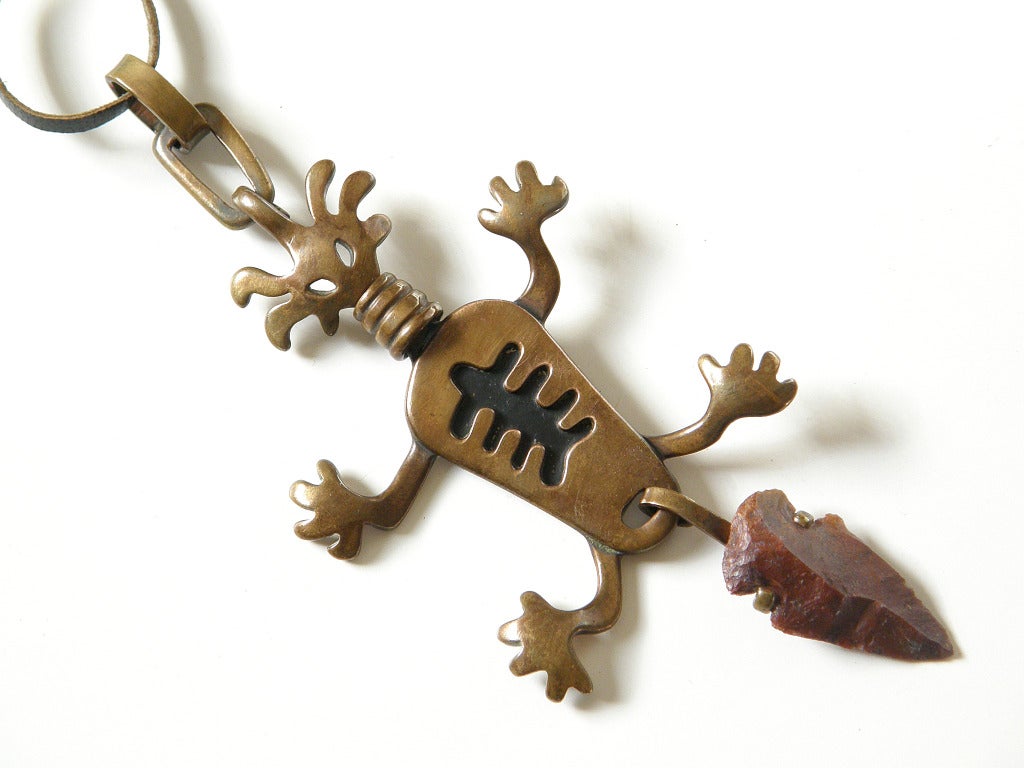 Copper pendant of a fantastical figure. This stylized creature is three-dimensional and has a wide neck ring, an abstract ribcage and a kinetic tail with what appears to be an Indian arrowhead mounted on it. The pendant hangs from a leather