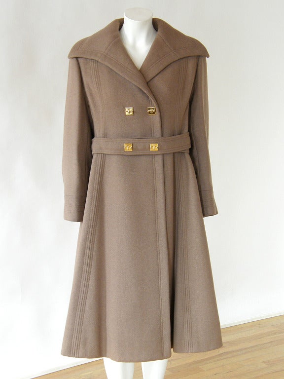 Exceptional wool coat by James Galanos. The subdued color and structured form are a great foil for the bold and unusual hardware on the coat, belt and cuffs. The stylized, door latch type hardware is both a little bit tough and a little bit glam.