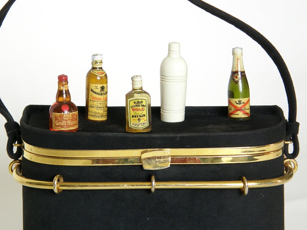 Rare cocktail bar shaped handbag by Anne-Marie. The bag is covered in black suede with a gold-plated brass bar rail and carved and decorated bakelite (or Catalin) liquor bottles and cocktail shaker. 

Anne-Marie had a shop within the famous Hotel