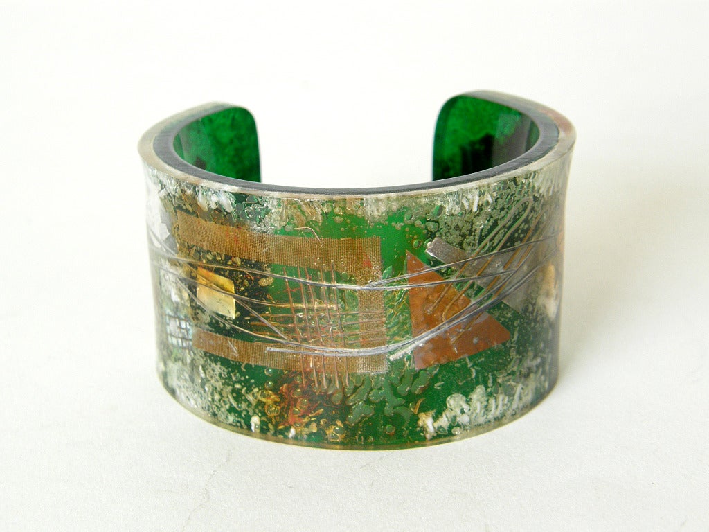 Laminated Plexiglas cuff bracelet by artist Zahara Schatz. The abstract design on the bracelet was created by laminating bits of foil, wire, screening, etc. between two pieces of plexiglas or lucite. The top layer is clear, and the background layer