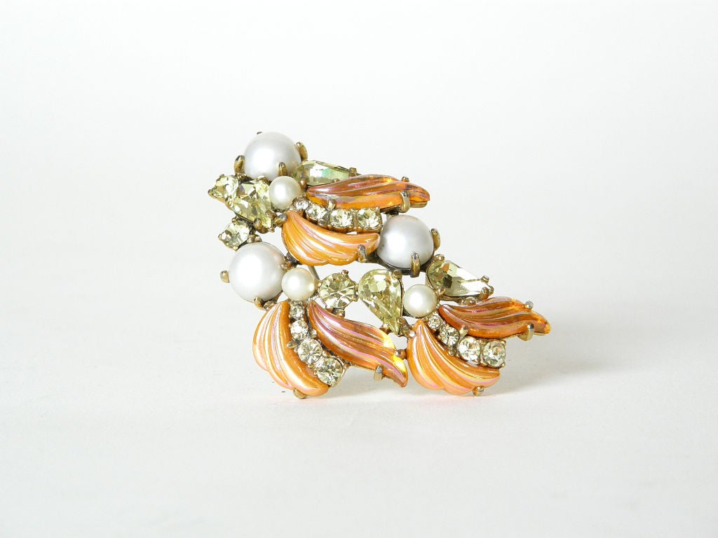 This Schiaparelli pin is great for summer. It is set with faux pearls, pale yellow green faceted rhinestones and curvy orange molded glass stones. Some of the orange stones are translucent and some of them are opaque. They all have a pink iridescent