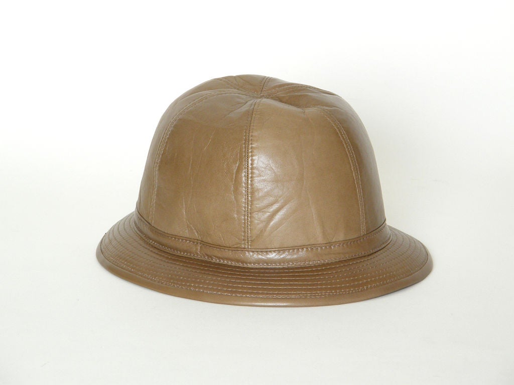 This chic Gucci leather hat appears unworn. It is made of a soft, light brown leather with a cloth lining and Gucci's classic gold-plated bridle hardware accenting the slender band. The style is a cross between a bucket hat and a pith helmet. I