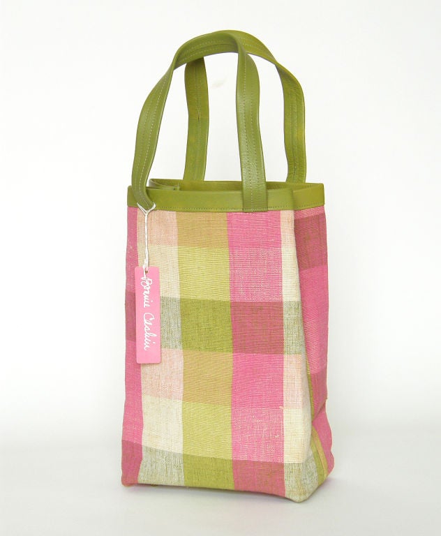 This is a rare, early Bonnie Cashin tote bag. It has an unusually tall and narrow shape. The body of the bag is covered in a lovely pink, green and cream colored plaid. The leather color ranges from avocado to light olive green. The colors appear