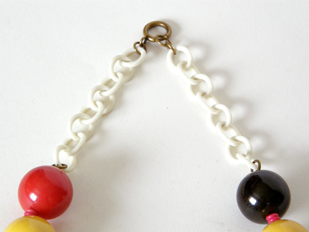 Playful beaded necklace in bakelite and celluloid. The red, yellow and dark green (almost blackish) bakelite beads have a rich patina. They're separated by pinkish red twisted celluloid spacers and hang from a creamy white celluloid chain.

beads