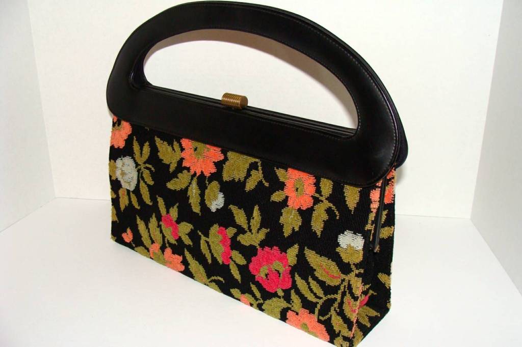 Large, over sized clutch with floral decoration on black background.

Interior lined with black fabric and has one zippered pocket.

Signature label remains below the pocket.

This is a great accessory that can transform a simple,