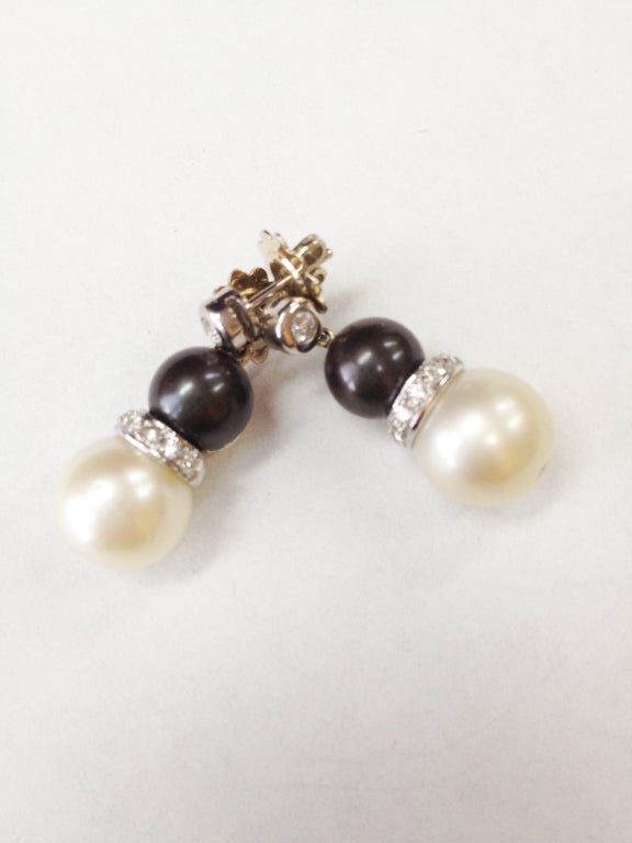 Stunning Black and White Cultured Pearl Diamond Earrings. Each earring comprising: bezel set diamond, weighing approx .10ct suspending a black Tahitian pearl, measuring approx. 9mm, and a white cultured pearl, measuring approx. 11.5mm; inter-spaced