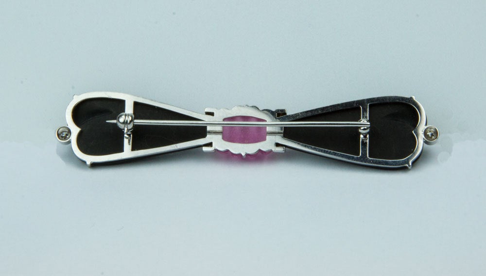 Beautiful black onyx ribbon bow pin centered by a ribbed pink tourmaline, accented with twelve brilliant-cut diamonds (including one each end), mounted in 14k white gold; handmade; approx. size: 2 
