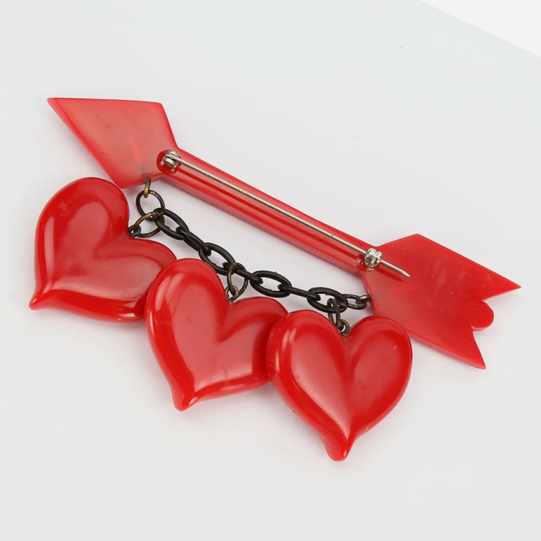 Red Bakelite 1940's-1950' arrow brooch pin with three Bakelite hearts suspended across by black chain.