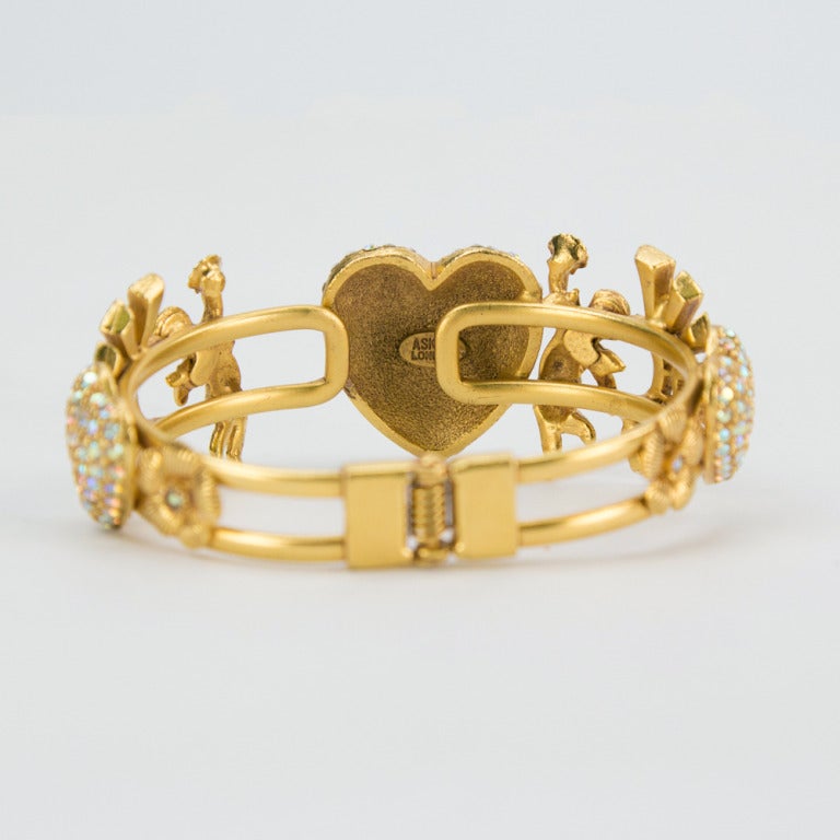 Askew London hinged Clamper Cuff Bracelet; golden winged cherub nymphs holding up sea shells on either side of the center heart, paved in Swarovski Aurora Borealis crystals; inter-spaced with star burst designs, more hearts- all paved with those