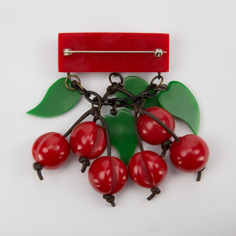 Fabulous Art Deco Celluloid Galalith Red Cherry pin; six carved red cherries and four green leaves dangling freely from a red Bakelite bar pin and black link chain. Go from Day to Night in Style and Grace!