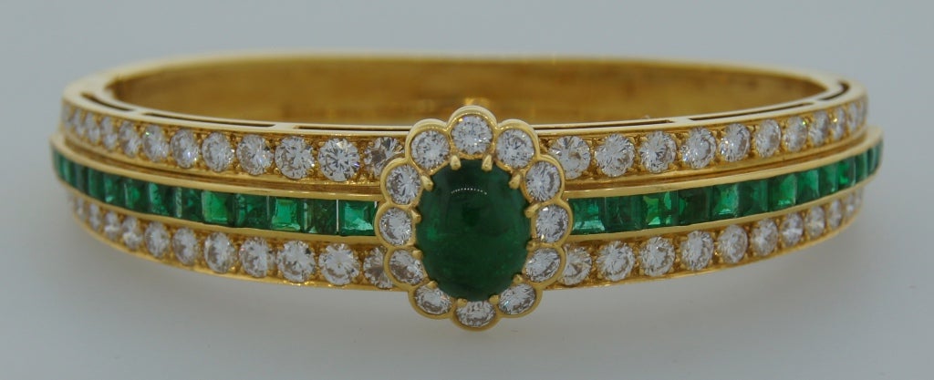 Elegant and feminine bangle bracelet created by Van Cleef & Arpels in France in the 1980's. Features a beautiful cabochon emerald framed in diamonds and accented with emeralds and diamonds. The bangle encrusted with 28 table cut emeralds and 52