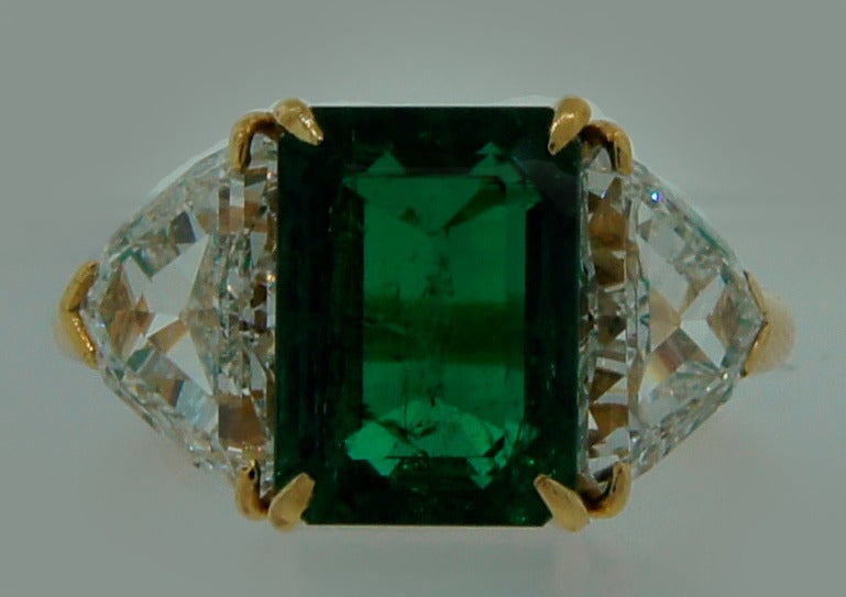 Timeless and classy three-stone ring created by Harry Winston in 1968. Features a 3.58-ct Colombian emerald flanked by a pair of trillion cut diamonds (total weight 2.36 carats, J color, VS1 clarity) mounted in 18k yellow gold. The emerald is