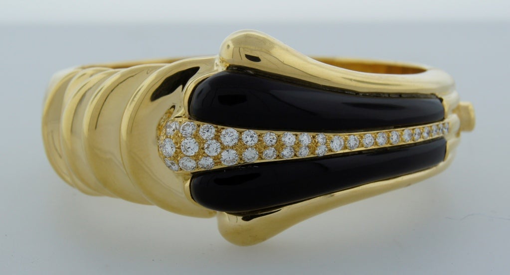 Chic and bold bangle created by Van Cleef & Arpels in New York in the 1970's. Strong architectural design, good volume and perfect proportions. Made of 18k yellow gold, black onyx and accented with round brilliant cut diamonds. 
Fits up to 7