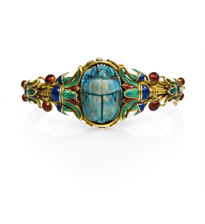 An antique gold and enamel scarab bracelet in the Egyptian Revival style with multicolored enamel lotus leaves centering on a blue faience scarab, in 18k. Marcus & Co. United States.