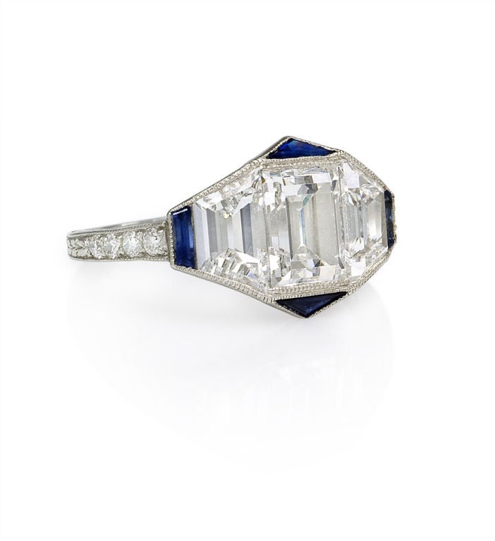 An Art Deco emerald cut diamond ring flanked by two trapezoid-cut diamonds, with four sapphire accents, set in platinum. Approximate total weight of center diamond: 1.24 carats, Color: H/I, Clarity: VS1. Approximate total weight of all diamonds,