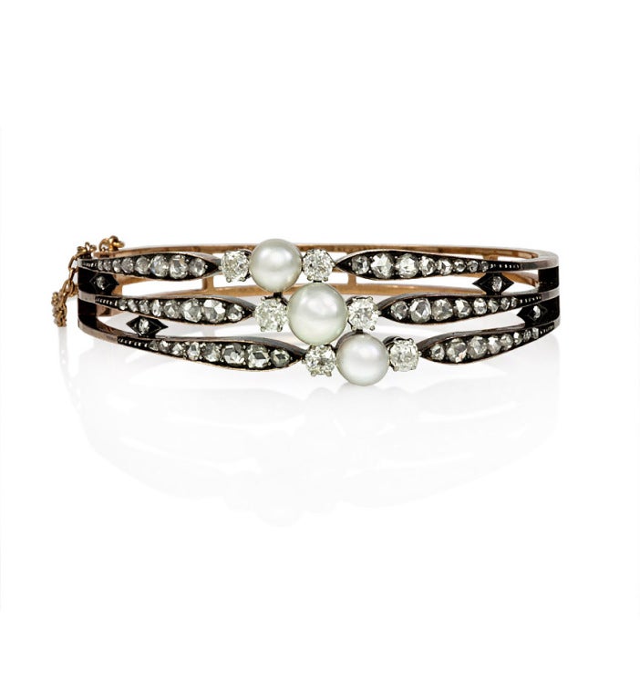 An antique diamond and pearl bangle bracelet centering on diagonally-set pearls with three tapering rows of old mine and rose cut diamonds, in silver and 18k gold.  French import marks.  Dimensions: 6 1/2