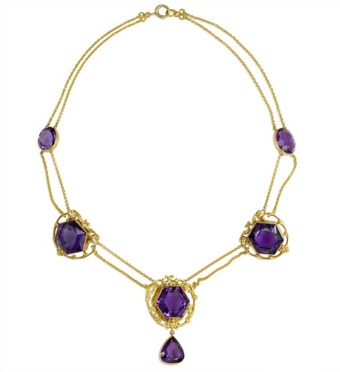 An Art Nouveau amethyst and gold necklace composed of three hexagonal-cut amethysts with two bezel-set amethysts on a two-row festoon chain, suspending a pear-shaped amethyst pendant, in 14k.