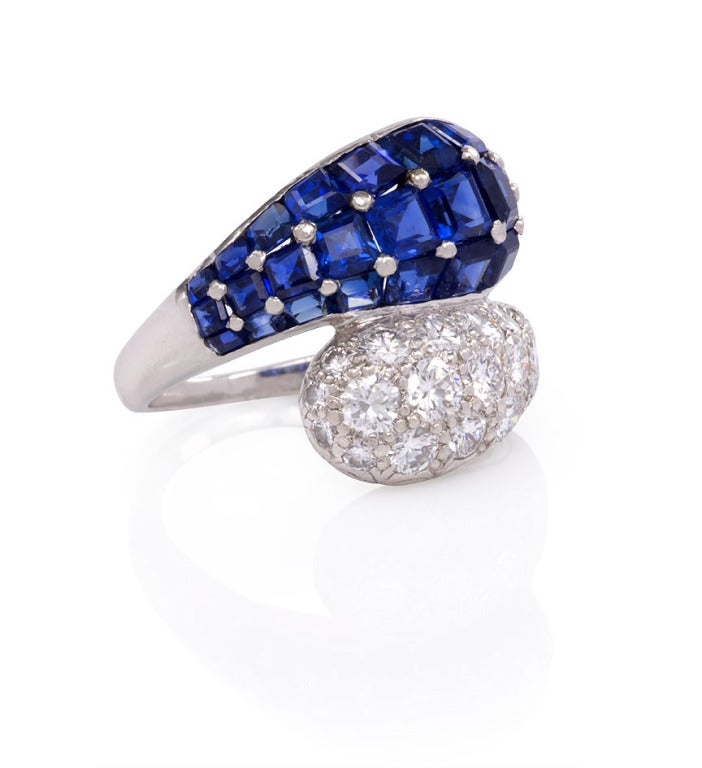 A diamond and sapphire ring of bombé crossover design, with bead-set square sapphires and brilliant cut diamonds, in platinum.  Oscar Heyman Bros. #61292.  Current ring size: slightly less than 5 1/2.