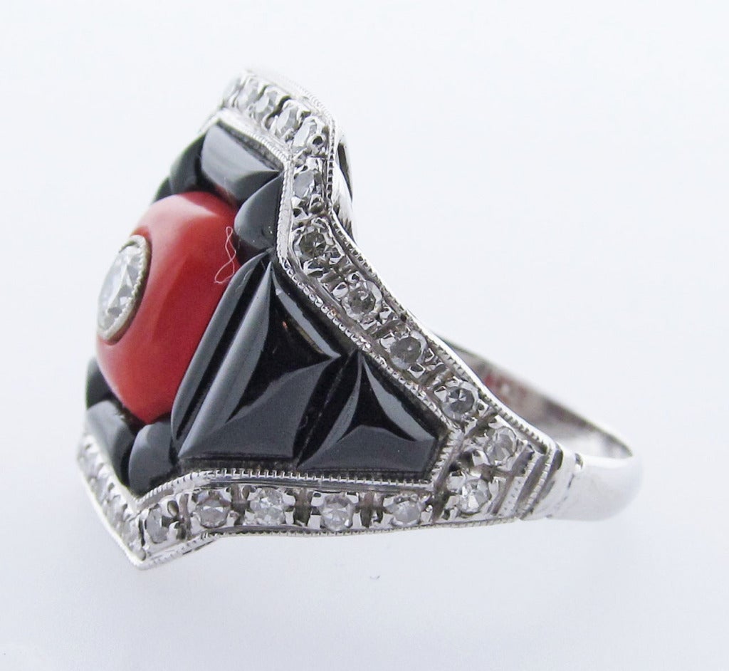 18kt. handmade white gold millgrained onyx, coral and diamond ring.  A round brilliant cut diamond bezel set  in the center weighing approx. .25 cts. and edged with 34 round single cut diamonds totaling approx. .40 cts. The ring is size 7 and may be